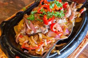 Close-up of beef fajitas with grilled sliced meat vegetables, herbs and onions, on a black stone plate
