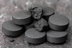 Close up of black tablets of activated carbon on a dark background (Flip 2020)