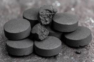 Close up of black tablets of activated carbon on a dark background