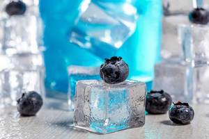 Close-up of blueberries on ice cube with blue cocktail behind