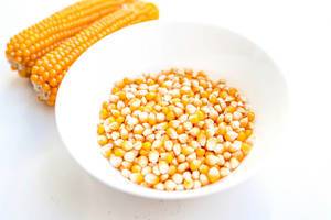 Close up of bowl of unpopped popcorn kernels on white background
