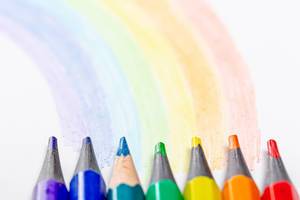 Close-up of colored pencils and a painted rainbow on a white background