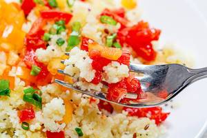 Close up of cooked porridge couscous with vegetables on a fork
