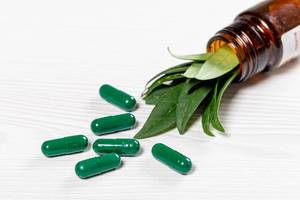 Close-up of green medical capsules with fresh green leaves in a glass bottle (Flip 2019)