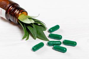 Close-up of green medical capsules with fresh green leaves in a glass bottle
