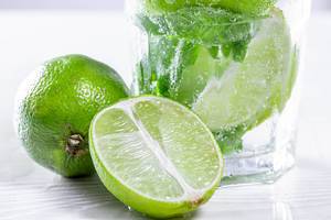 Close-up of half and a whole a lime and a glass of Mojito behind