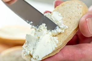 Close-up of hand spread cheese on bread with a knife