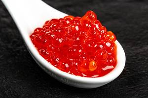Close-up of red caviar in a white spoon on a black background