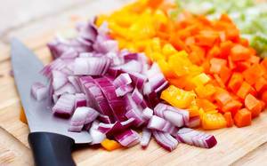 Close Up of Red Onion, Yellow Bell Pepper and Carrot Vegetables cut in Cubes with Kitchen Knife on Wooden Cutting Board
