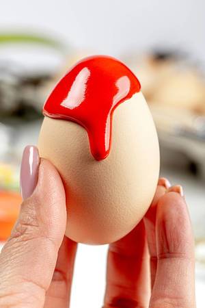 Close-up of red paint flowing down a chicken egg in a female hand
