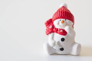 Close Up of Small Snow Person Decoration with Red Hat and Scarf on white Background