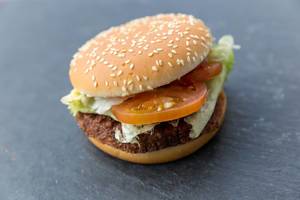 Close-up of the meatless burger "Big Vegan TS" by McDonalds on dark background with soy-patty wheat protein, green salad and sesame seeds