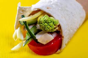 Close-up of vegetables and meat wrapped in pita on yellow background