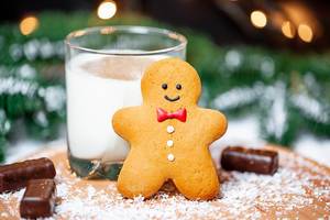 Close Up Photo of a Gingerbread Man leaning on a Glass of Milk with Chocolate Pralines on Christmas Background