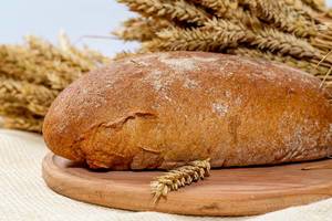 Close Up Photo of a Loaf of Rye Bread on a Wooden Cutting Board with barley spikes