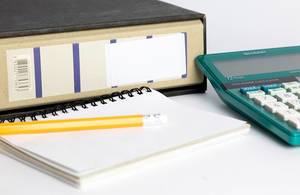 Close Up Photo of Accounting Tools such as Pencil laying on a blank Notebook next to a Calculator and a Folder on white Background