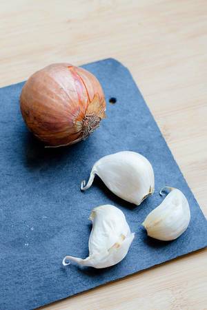 Close Up Photo of Cloves of Garlic next to Onion on Black Board