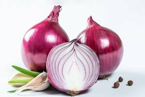 Close Up Photo of Garlic and Pepper next to Full and Halved Red Onion on White Background