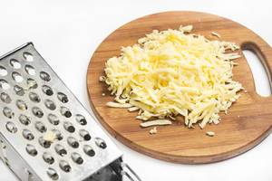 Close Up Photo of Grated Cheese on Wooden Cutting Board next to Grater on White Background