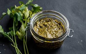 Close Up Photo of Homemade Green Pesto in a Glass Jar with Parsley on Dark Background