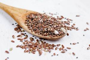 Close Up Photo of Linseeds on a Wooden Spoon on White Wooden Background