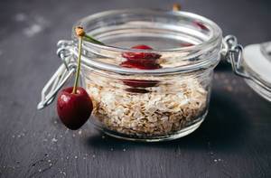 Close Up Photo of Oatmeal in a Glass Container with Cherries on Black Wooden Table