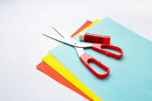 Close Up Photo of Scissors and Glue laying on colorful Craft Paper on White Background