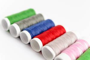 Close Up Photo of Sewing Thread in different colors laying next to each other on white Background