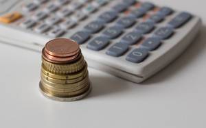 Close Up Photo of Stack of Coins with Calculator in the Background