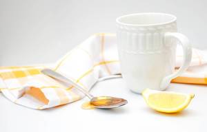 Close Up Photo of White Cup next to a Spoon with Honey and Piece of Lemon on white Background