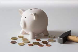 Close Up Photo of White Piggy Bank with Coins around it and Hammer next to it on White Background