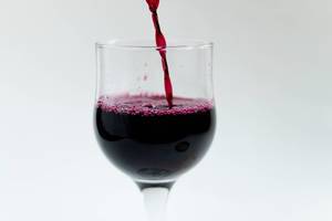 Close Up Photo of Wine Glass being filled up with Red Wine on White Background