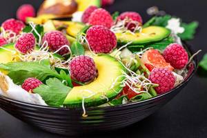Close-up, salad with avocado and raspberries in a black bowl. The concept of vitamins, taking care of the figure (Flip 2020)