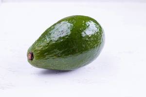 Close up shot of green avocado laying on a white table