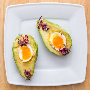 Close Up Top View Food Photo of Halved Avocado with Soft Boiled Egg on a White Plate