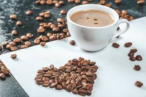 Close Up View of Coffee Beans in Heart Shape and a Cup of Coffee on a White Board