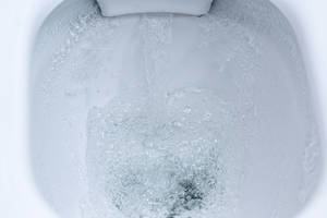 Closeup view of a flushing white toilet. The water swirls in the toilet bowl