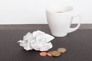 Coffee cup with receipt and coins on table