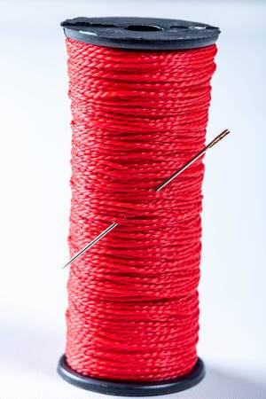 Coil of red thread with needle on white background