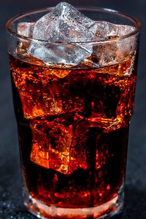 Cola with ice in glass on black background