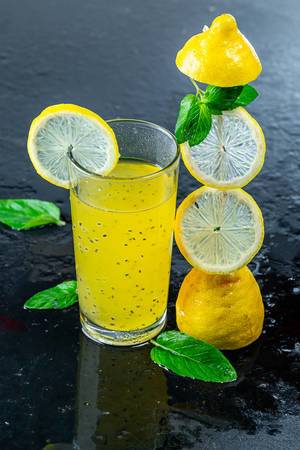 Cold yellow drink with fresh lemon and mint leaves on black background