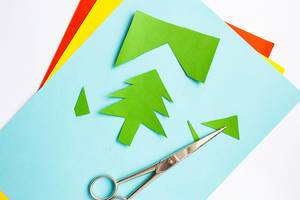 Colorful craft paper with christmas tree cutout and scissors on white background