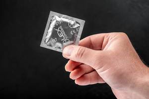 Condom in the hand of a man on a black background. The concept of individual protection