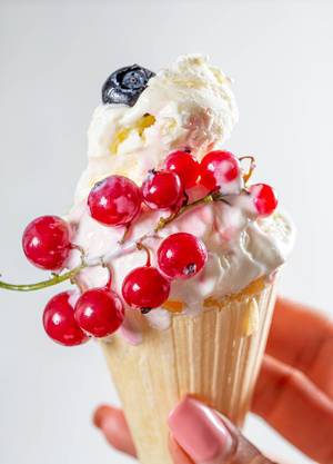Cone with vanilla ice cream and fresh red currant berries in a woman