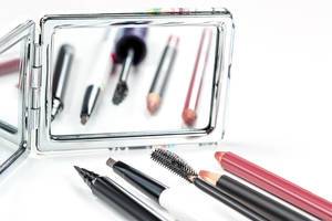 Cosmetic pencils, eyeliner and carcasses on the background of a mirror