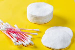 Cotton swabs and cotton rounds for face care on a yellow background