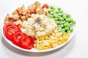 Couscous with Chia seeds, young peas, corn, tomatoes and baked chicken on a white plate