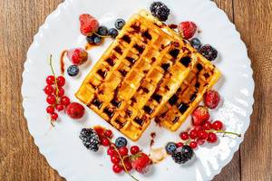 Crispy Belgian waffles with chocolate topping and ripe berries on a white plate. Top view