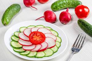 Cucumber, radish and tomato sliced on a plate on a white table with ingredients