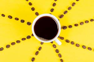 Cup of black coffee on a yellow background with coffee beans, top view